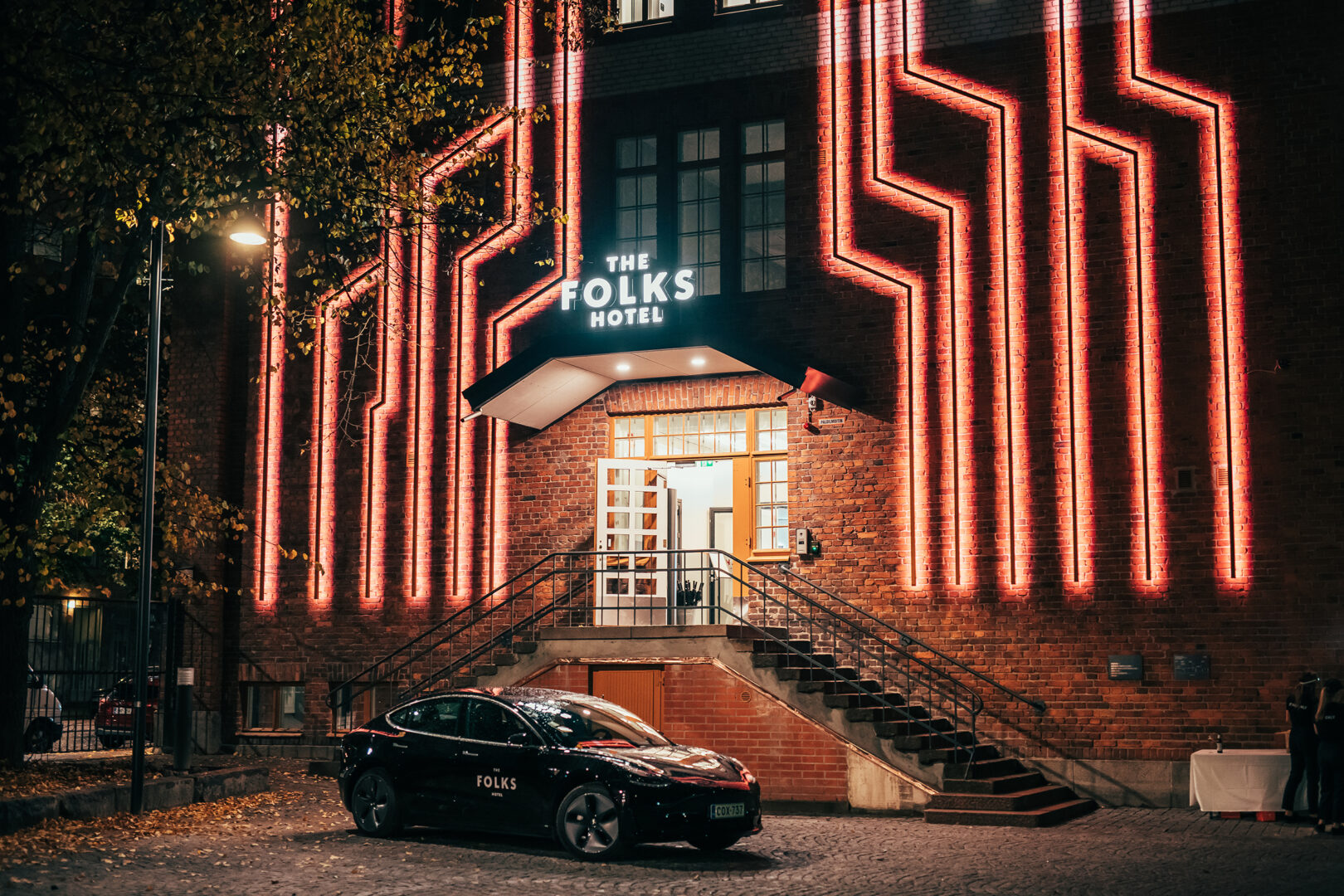 Kuvassa on The Folks Hotel Konepajan sisäänkäynti. Tiiliseinässä loistavat valot, jotka näyttävät junan raiteilta ja muistuttavat hotellin historiasta.